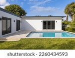 Small photo of Beautiful backyard of elegant and modern house in the Nautilius neighborhood of Miami Beach, swimming pool, short grass, trees and tropical plants, blue sky in the background