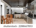 Modern outdoor kitchen and. luxury with grill, stove, extractor hood, wooden ceiling with fan, wooden tables and benches, chop tap, tiled wall.
Located in Coral Gables, Miami, FL, USA