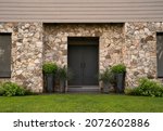 Modern architecture. Residential facade design. Closeup view of new house iron front door, stonewall and decorative plants Buxus sempervirens, also known as boxwood bush, growing in pots.
