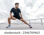 Small photo of A trainer in fitness clothes is a T-shirt, running sports shoes and a smart watch for sports. A strong man. A confident male athlete training does warm-up exercises.