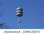 Small photo of Closeup Dutch Siren, air raid with antenna on a pole. A seagull on it. With green algae. Blue sky. Dutch national emergency signalling system. Spring April, Bergen, Netherlands.
