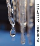 Small photo of Icicles in the rays of a winter sunset close up. Focus on the icicle. Drop of melt water in blur. Snow is melting. Vertical illustration on the theme of thaw and beginning of spring. Macro