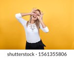 Small photo of Young beautiful caucasian woman showing ok sign gesture near eyes loke glasses wearing white shirt on isolated orange background