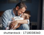 Small photo of Middle age Caucasian father kissing sleeping newborn baby girl. Parent holding rocking child daughter son in hands. Authentic lifestyle parenting fatherhood moment. Single dad family home life.