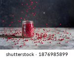 Red or pink peppercorns falling in a glass jar on grey textured table,  black background. Motion spices image. Copy space.