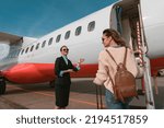 Small photo of Woman stewardess standing near airplane and inviting female passenger on board