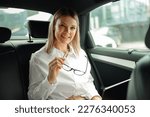 Pretty woman sales manager working on laptop sitting car backseat and looking at camera