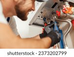 Small photo of Closeup of plumber using screwdriver while installing new steel hot water central heating system in apartment