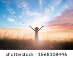 Surrender and praising concept: Silhouette of healthy Christian woman raised hands at meadow sunset background