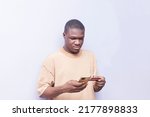 Small photo of unsmiling young black african man using mobile phone and card in hand for shopping online