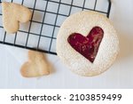 Close up of a single Linzer Cookie with heart shape cut out of biscuit and filled with red raspberry jam. Biscuits on cooling rack in heart shapes against white background.
Love, romance and valentine
