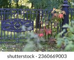 A view of a cast-iron lattice fence through which a young maple tree with crimson autumn leaves grows. Bokeh.