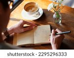 Small photo of Asian man writing diary book journal with cup of coffee and flowers on wooden table 1