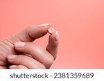 Small photo of Pink pill in woman hand on pink background. Medical concept of medicine treatment, vitamins, supplements, contraceptive pills or feminine drug addiction. Close up, selective focus.