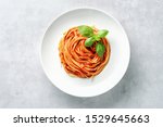 Top view of plate with spaghetti in tomato sauce and basil on white background