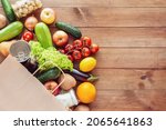Small photo of Paper grocery bag with fresh vegetables, fruits, milk and canned goods on wooden backdrop. Food delivery, shopping, donation concept. Healthy food background. Flat lay, copy space.