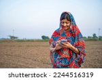Indian rural woman in traditional saree and using smartphone at agriculture field.