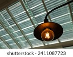 Small photo of An incandescent light bulb over a dining table in a cafe. The incandescent bulb contains a filament which gives off a glowing light when heated by an electric current.