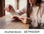 Girl holding a book wearing in warm wool pullover with red gel polish manicure. Wood retro background. Student woman concept.