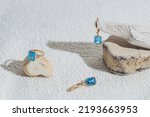 Small photo of Elegant jewellery set of gold earrings and ring with blue topaz on white background with stones and wood. Minimal style composition. Product still life concept