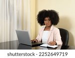 Small photo of woman makes annotation on her notebook at her workplace, young black woman looks at camera