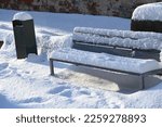 a snowy wooden park bench and a trash can
