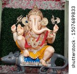 Small photo of statue of lord ganesh wearing gold jewellery, crown, holding modak, trident, trisul in his hands sitting on mouse rat isolated on colorful rose and green grass background. indian ganpati festival.