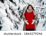 Young pregnant woman in winter clothes and red christmas sweater walking in the winter forest
