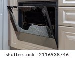 Opened broken oven door in the kitchen, side view, close-up. Broken glass from overheating. Broken glass from impact