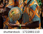 A closeup photo shows a drummer playing an African Shekere gourd percussion instrument while marching in a procession during a kente yam festival in Ghana, West African