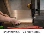 Small photo of Close-up hands of joiner, professional man hands using panel sizing saw woodworking machine or tool, knife sawing to cut wood board in small shop. Red pusher, tappet on the table. Workshop or garage