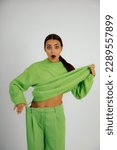 Small photo of Vertical shocked, dazed beauteous brunette woman with open mouth in big green costume presenting thin, slim sportive abdomen on white studio background. Swell build body, healthy dieting. Copy space