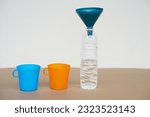 Blue and orange cups , bottle of water and funnel on the top. Concept, equipment for doing experiment, measuring liquid quantity.      