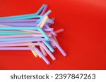 Colorful plastic drinking straws tubes for juice and cocktails, red background. Concept, single use equipment for drinking, but can use for diy crafts for decoration.      