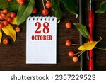 Small photo of calendar date on wooden dark desktop background with autumn leaves and small apples. October 28 is the twenty-eighth day of the month.
