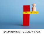 Small photo of Risk, failure, instability and downfall concept in business. Wooden doll standing on the edge of wooden tile. Blue background with copy space for text.