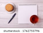 Small photo of a note book with empty space for writing, a pen and a tea cup with black tea and a plete with cookies. minimalism style. top view