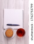 Small photo of a note book with empty space for writing, a pen and a tea cup with black tea and a plete with cookies. minimalism style. top view