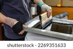 Small photo of silk screen textile printery. male hand with a squeegee. printing by silk screen method in a design studio. creating print on t-shirt in workshop. serigraphy production selective focus photo