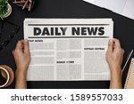 Small photo of Hands holding Business Newspaper and office supplies with notebook, hot coffee cup, glasses, books and accessories on black desk topview, Daily Newspaper mockup concept