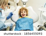 Cute young boy visiting dentist, having his teeth checked by female dentist in dental office