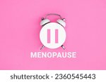 Small photo of White vintage alarm clock with an inscription MENOPAUSE on pink background.