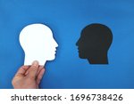 White head profile silhouette facing black shadow in blue background. Face fears, dark side, bipolar identity concept.