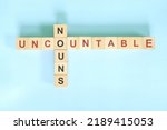 Small photo of Uncountable nouns concept in English grammar noun education. Wooden block crossword puzzle flat lay in blue background.