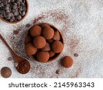 Chocolate truffles covered with cocoa powder in brown wooden bowl with dark chocolate pieces and cocoa powder in wooden spoon. Gray background. Top view table. Delicious candies, tasty dessert.