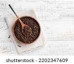 Dried cloves in wooden bowl on white wooden table. Condiment, spice, flavouring and cooking ingredient. Top view food. Copy space. Wooden spoon, kitchen textile napkin.