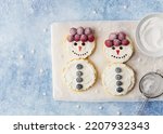 Funny snowmen made of pancakes, ricotta (cream cheese) spread, fresh berries and chocolate. Top view. Blue background. Christmas and new year breakfast concept. Festive winter dessert for kids.