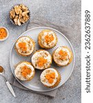 Small photo of Carrot (pumpkin) cupcakes with swirls of sliced carrot, chopped nuts, cream and cinnamon powder. Festive autumn baking. Seasonal cooking. TCloseup view. Decorated vegetable muffins on plate.