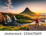 Panorama landscape of sunrise over volcanic Kirkjufell mountain with Kirkjufellsfoss waterfall and photographer man standing in summer at Snaefellsnes peninsula, Iceland