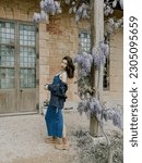 Small photo of a woman in denim dress and embroidered jacket by blooming flowers near Marie Antoinette's little house